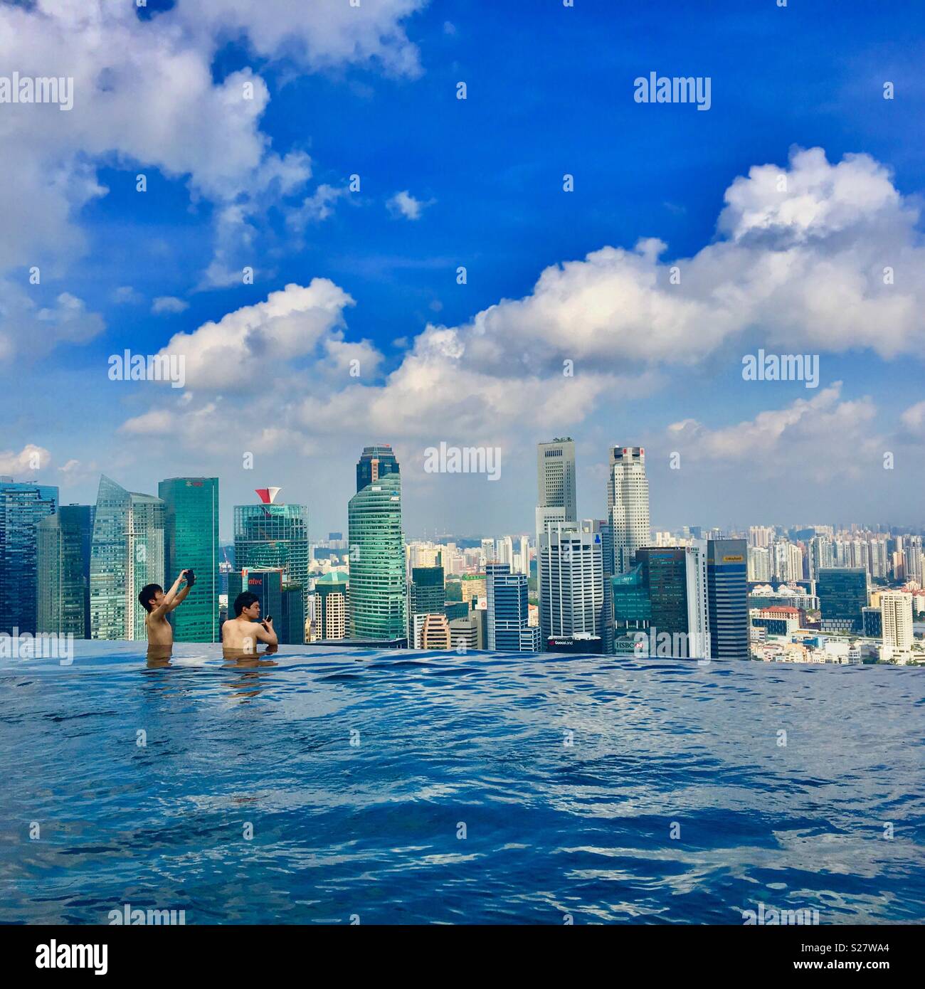 Marina Bay Sands Hotel pool in Singapore with two men taking photos and skyscrapers in background - Smartphone Captured Stock Image