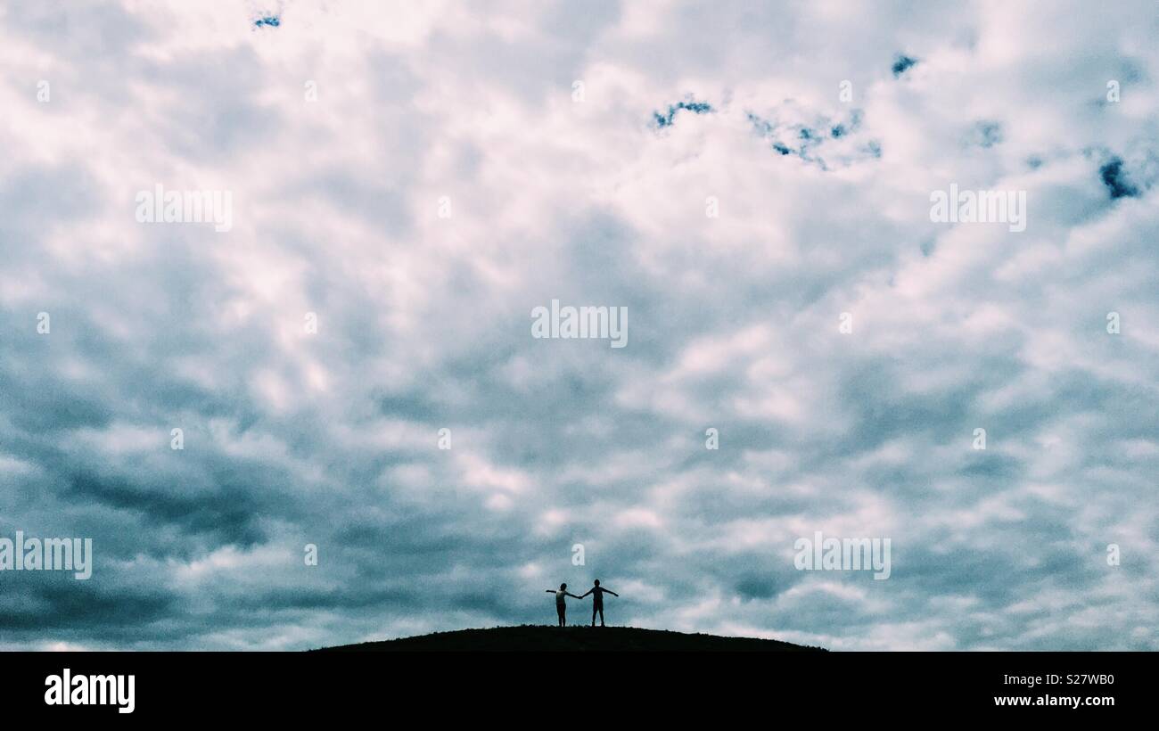Two girls at the top of a hill with cloudy sky. Stock Photo