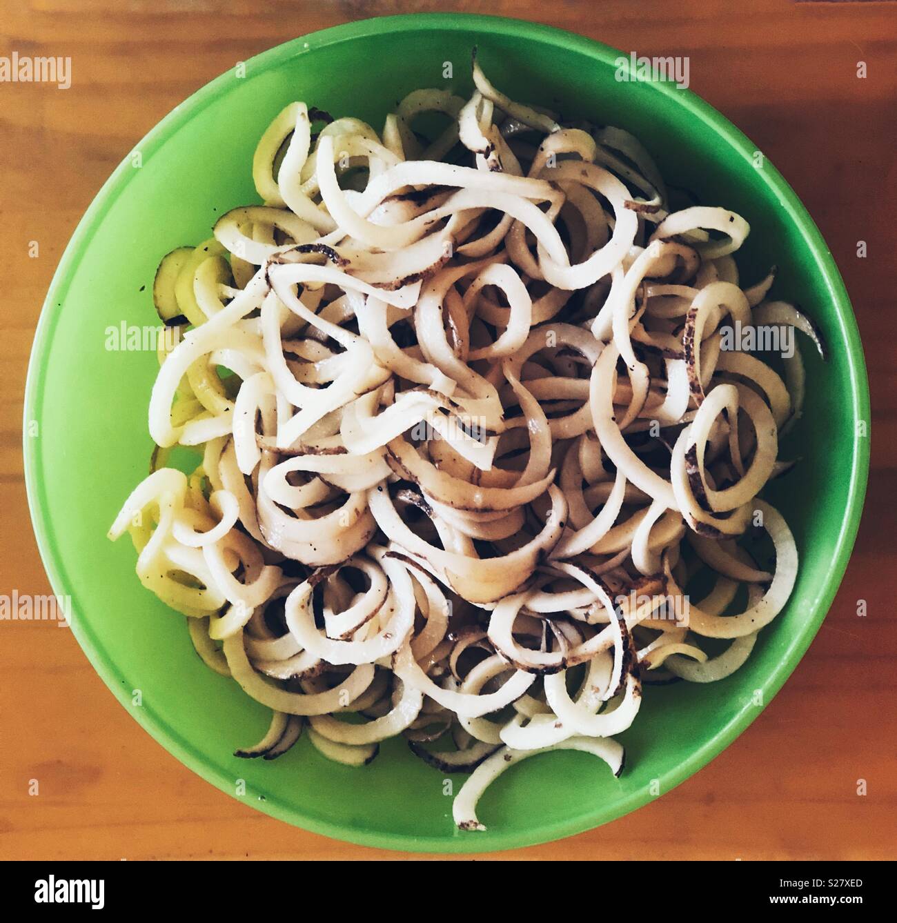 Spiralized raw white potatoes with skins in a green plastic bowl with orange background - Smartphone Captured Stock Image