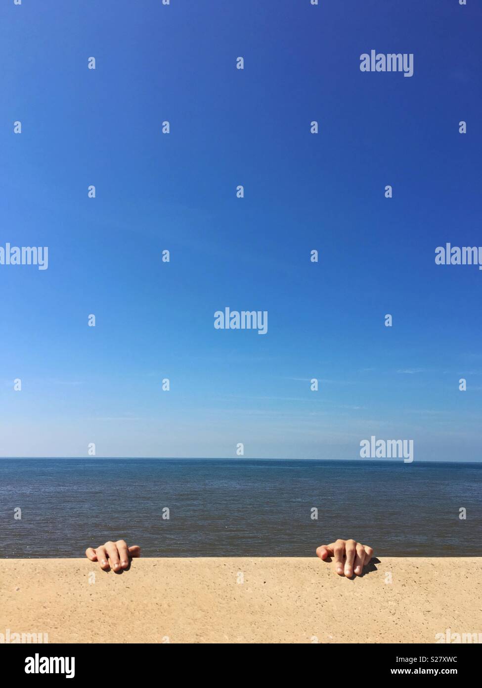 Two hands grasping wall with sea and blue sky as background Stock Photo