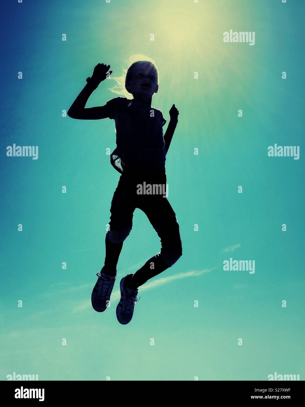 Girl jumping in silhouette against the sun and sky with grunge filter treatment Stock Photo