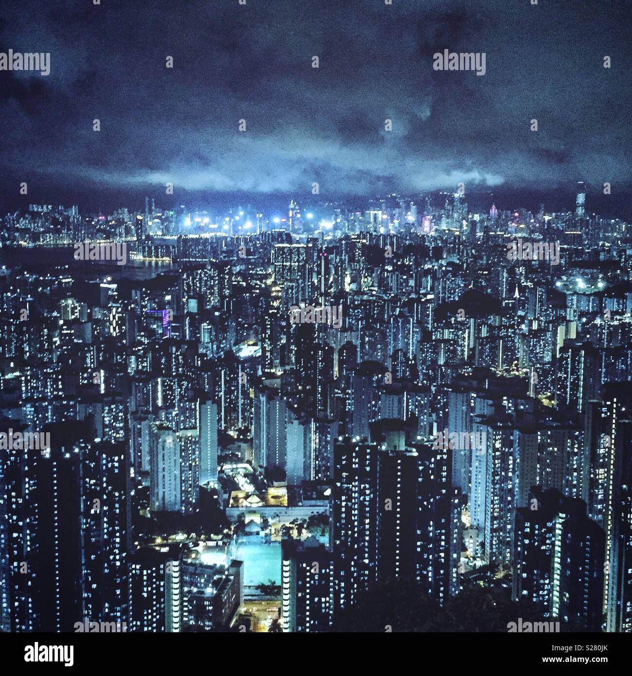 The bright lights of Hong Kong Island and Tsim Sha Tsui viewed across the high density urban landscape of the Kowloon Peninsula from the old Sha Tin Pass Road, Hong Kong (cool tone) - Smartphone Captured Stock Image