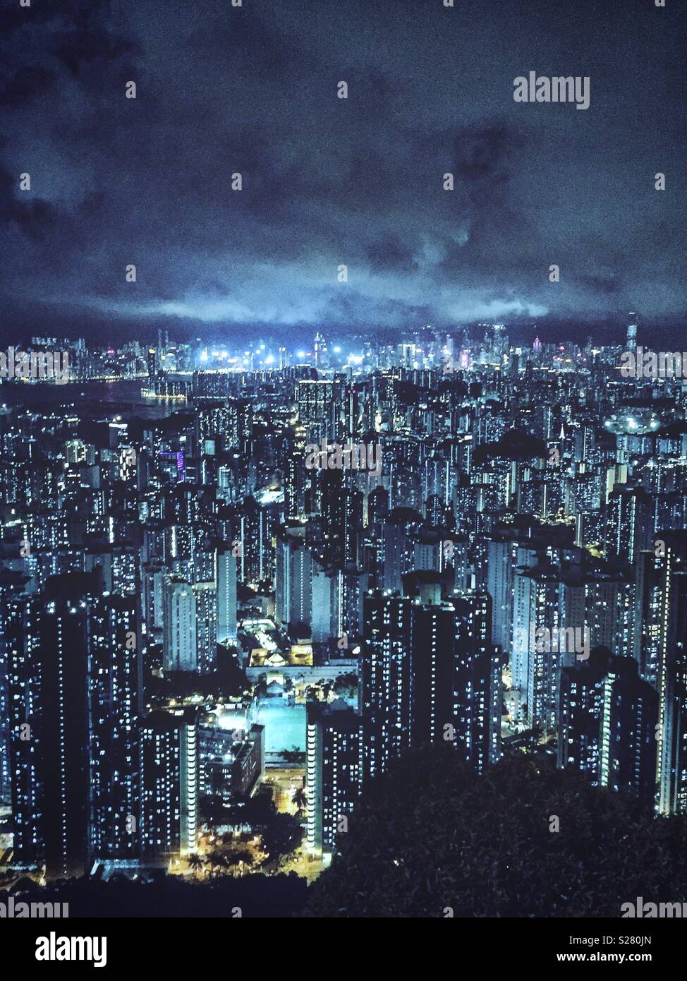 The bright lights of Hong Kong Island and Tsim Sha Tsui viewed across the high density urban landscape of the Kowloon Peninsula from the old Sha Tin Pass Road, Hong Kong (cool tone) Stock Photo