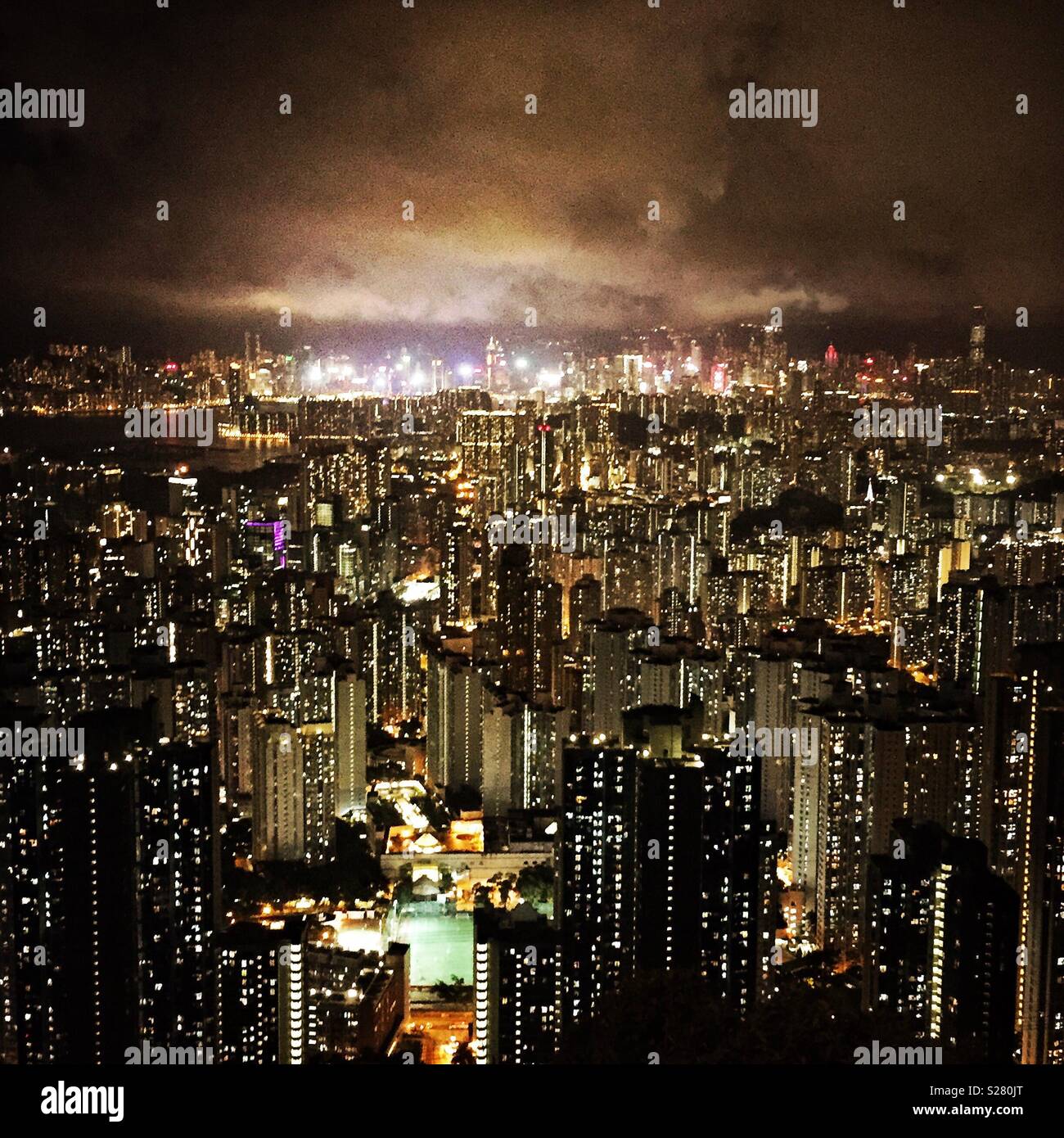 The bright lights of Hong Kong Island and Tsim Sha Tsui viewed across the high density urban landscape of the Kowloon Peninsula from the old Sha Tin Pass Road, Hong Kong (warm tone) Stock Photo