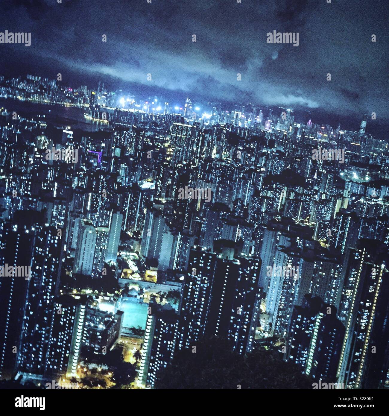 The bright lights of Hong Kong Island and Tsim Sha Tsui viewed across the high density urban landscape of the Kowloon Peninsula from the old Sha Tin Pass Road, Hong Kong (cool tone) - Smartphone Captured Stock Image