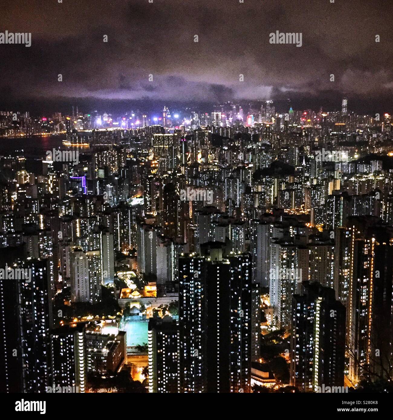 The bright lights of Hong Kong Island and Tsim Sha Tsui viewed across the high density urban landscape of the Kowloon Peninsula from the old Sha Tin Pass Road, Hong Kong (neutral tone) Stock Photo