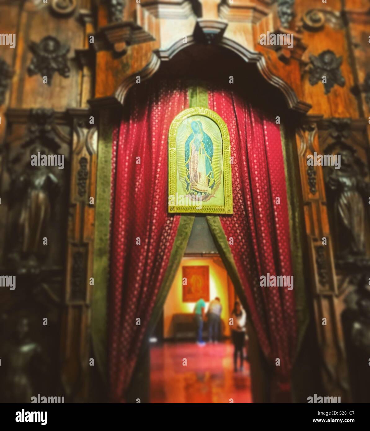 An image of Our Lady of Guadalupe is shown in a door decorated with a red curtain in the Basilica of Our Lady of Guadalupe in Mexico City, Mexico Stock Photo