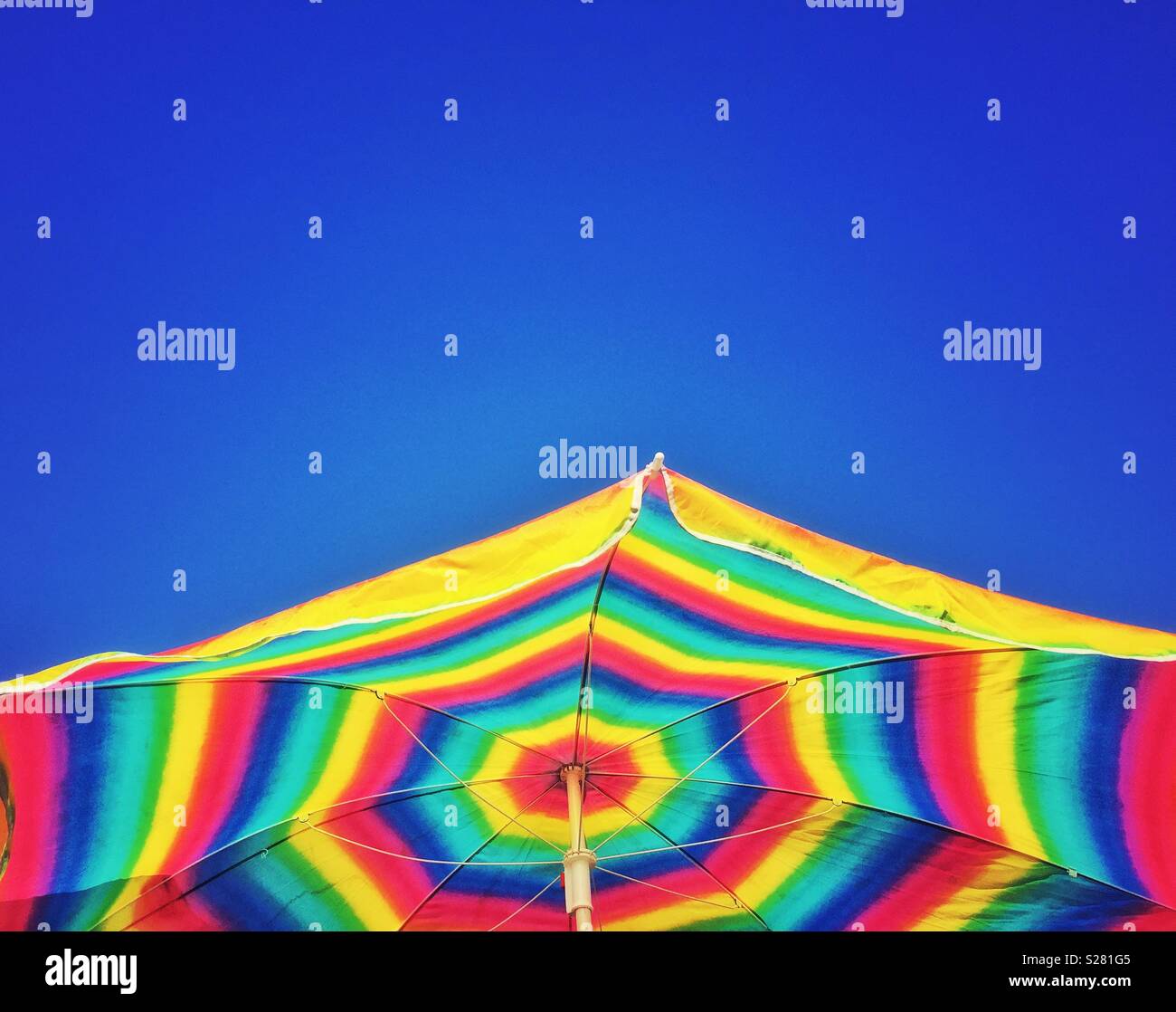 Bright multicolored beach umbrella against a clear blue sky. - Smartphone Captured Stock Image