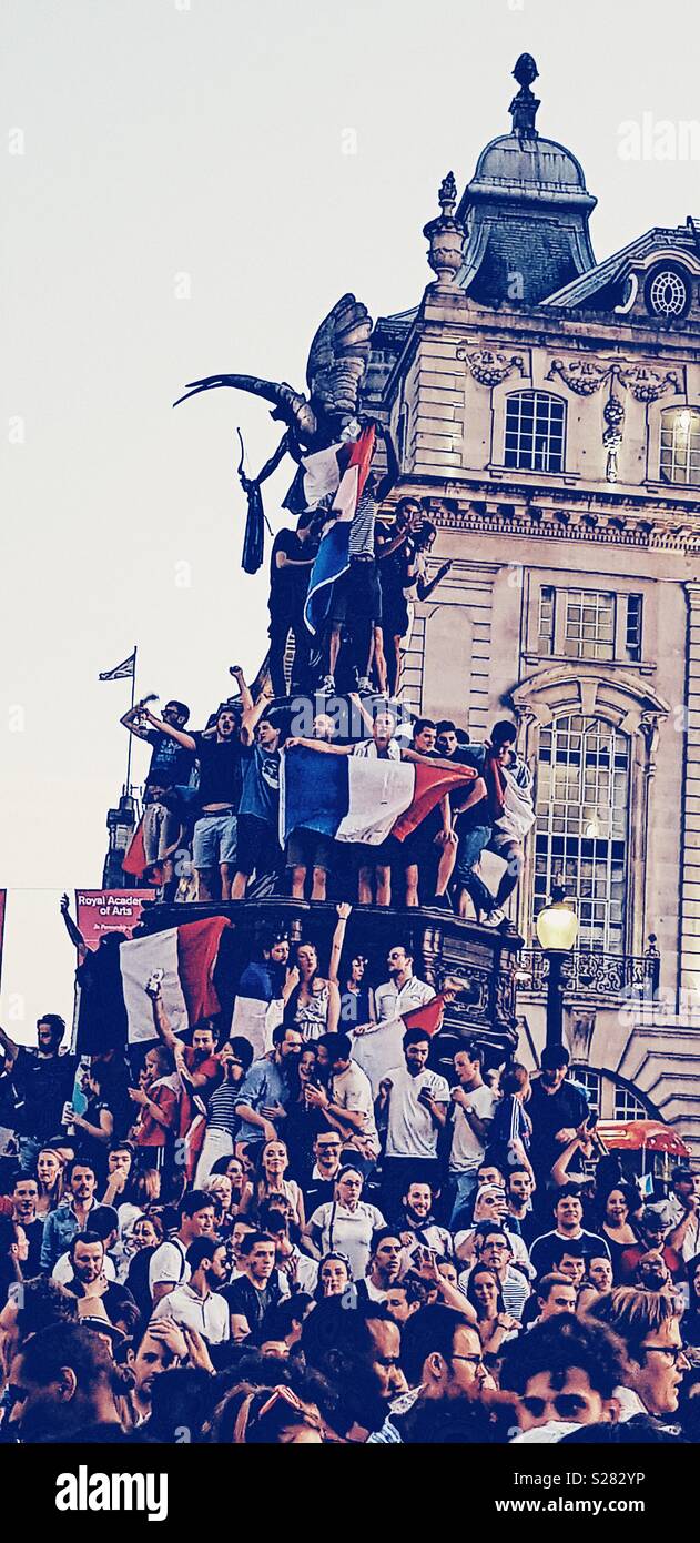 French football fans with the French flag (Tricolour) climbing Eros statue to celebrate France’s 2018 World Cup win, Piccadilly Circus, London - Smartphone Captured Stock Image