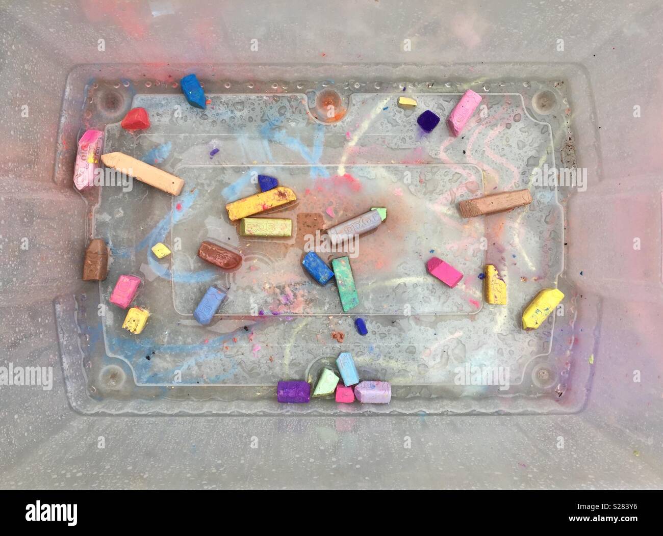 Sidewalk chalk in a plastic bin with the colors running in the rain - Smartphone Captured Stock Image