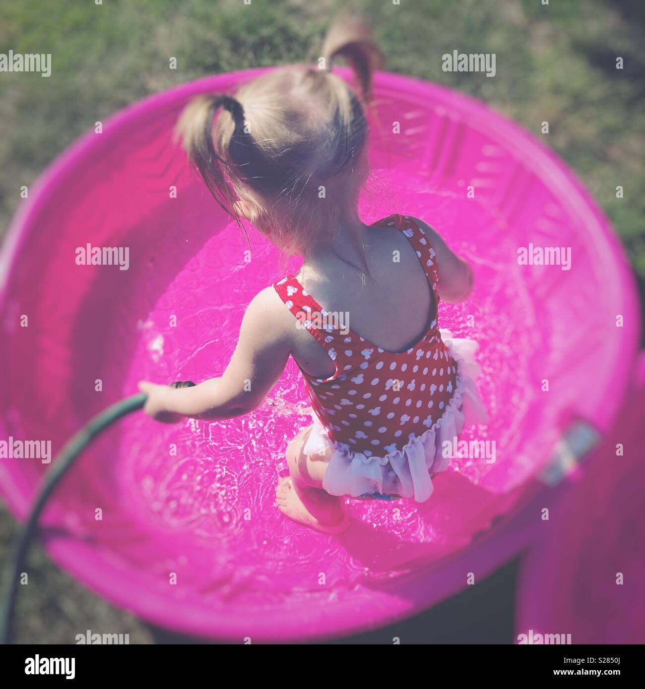 Toddler girl with pigtails filling a kiddie pool with a hose Stock Photo