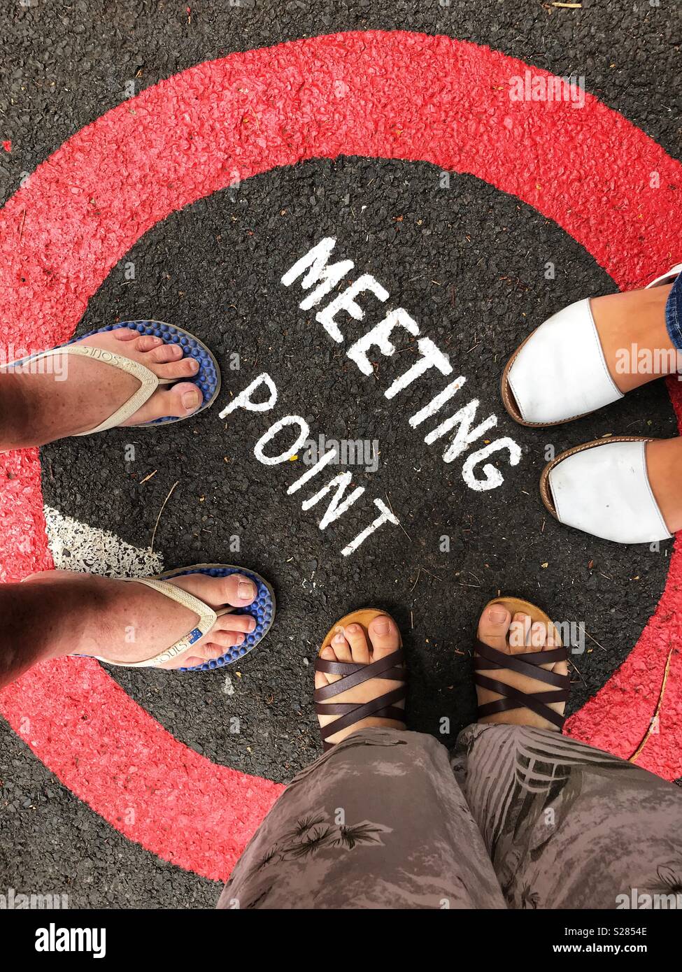 POV, the feet of three people, standing on a Meeting Point sign painted on the road, Funchal, Madeira, Portugal - Smartphone Captured Stock Image