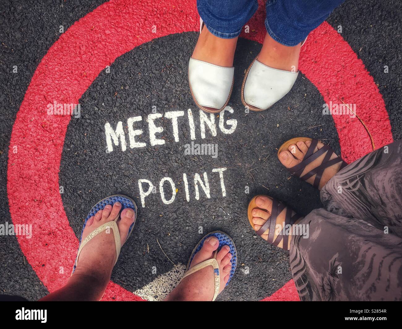 POV, the feet of three people, standing on a Meeting Point sign painted on the road, Funchal, Madeira, Portugal - Smartphone Captured Stock Image