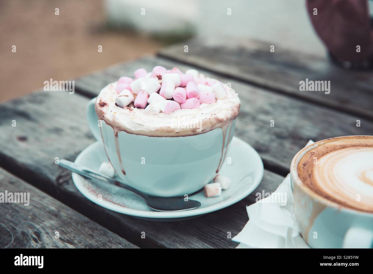 A luxurious hot chocolate drink in a cup and saucer with whipped cream and marshmallows outdoors - Smartphone Captured Stock Image