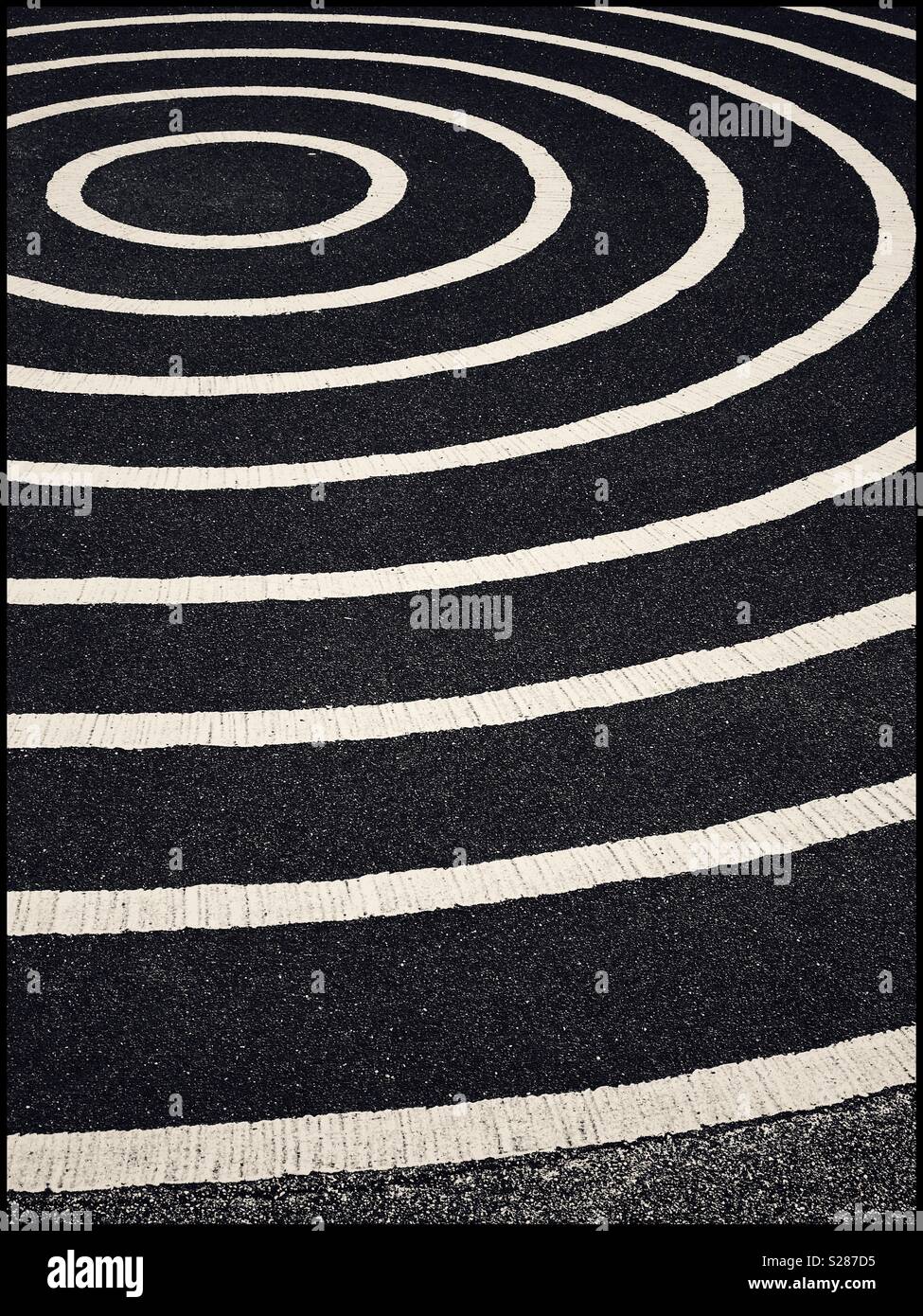 A graphic, monochrome image of concentric circles, painted onto a large area of tarmac (asphalt). An image with multiple potential uses. Photo Credit - © COLIN HOSKINS. - Smartphone Captured Stock Image