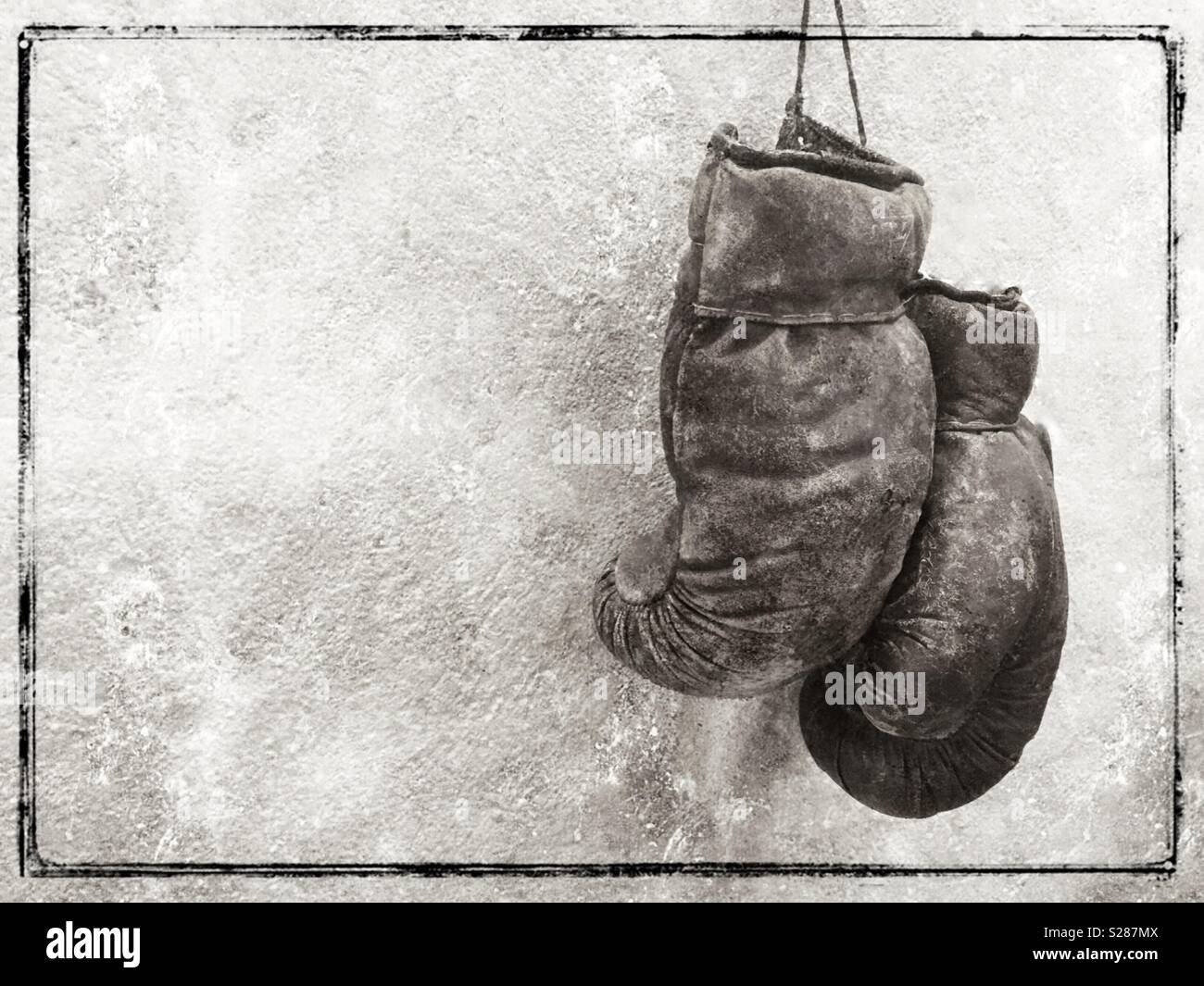 Black and white image of old worn boxing gloves hanging on a