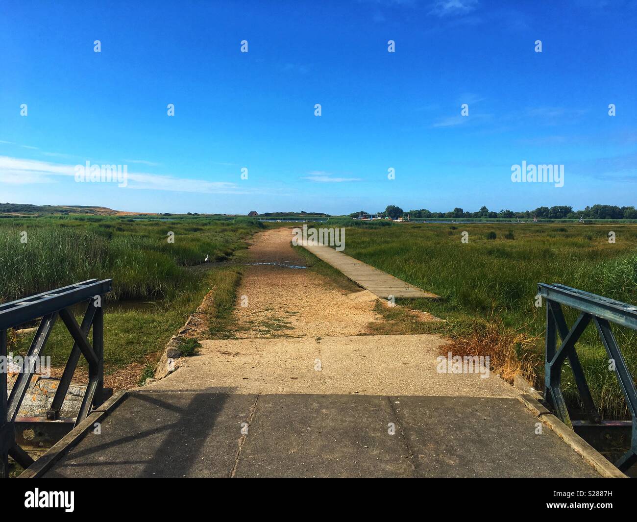 Bridge and pathway going into the distance amongst the marshes towards the sea Stock Photo