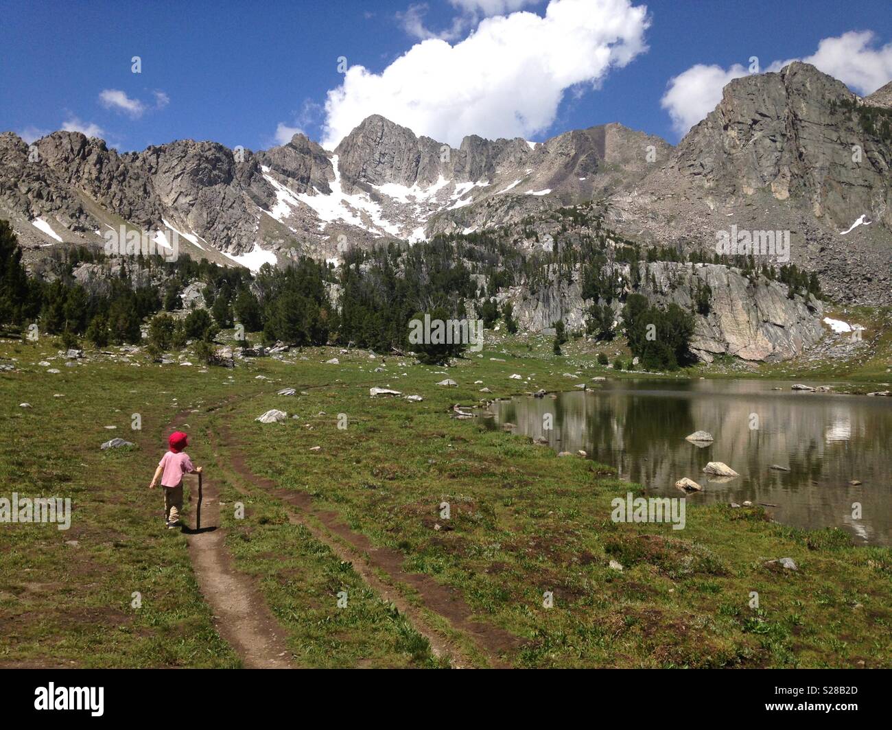Young child hiking in mountains walking past a mountain lake Stock Photo