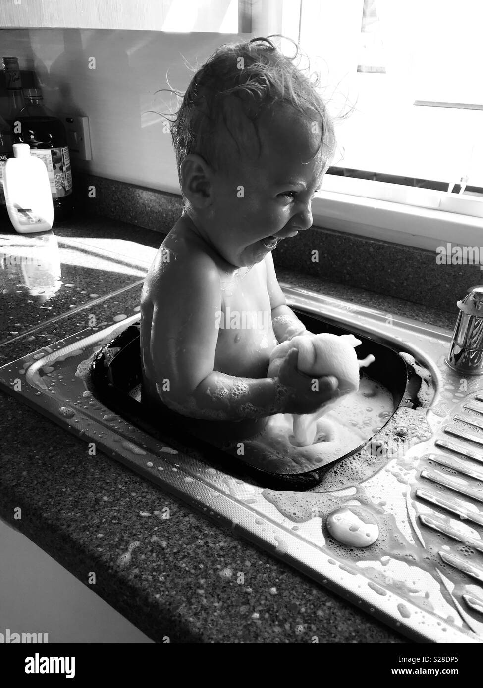 Baby boy having bath in kitchen sink Stock Photo
