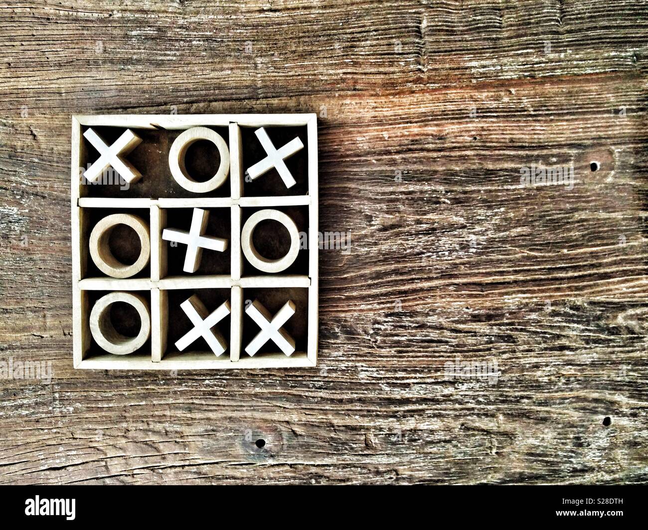 Wooden tic-tac-toe or noughts and crosses game on a grainy tabletop with copy space. Crosses win. Stock Photo