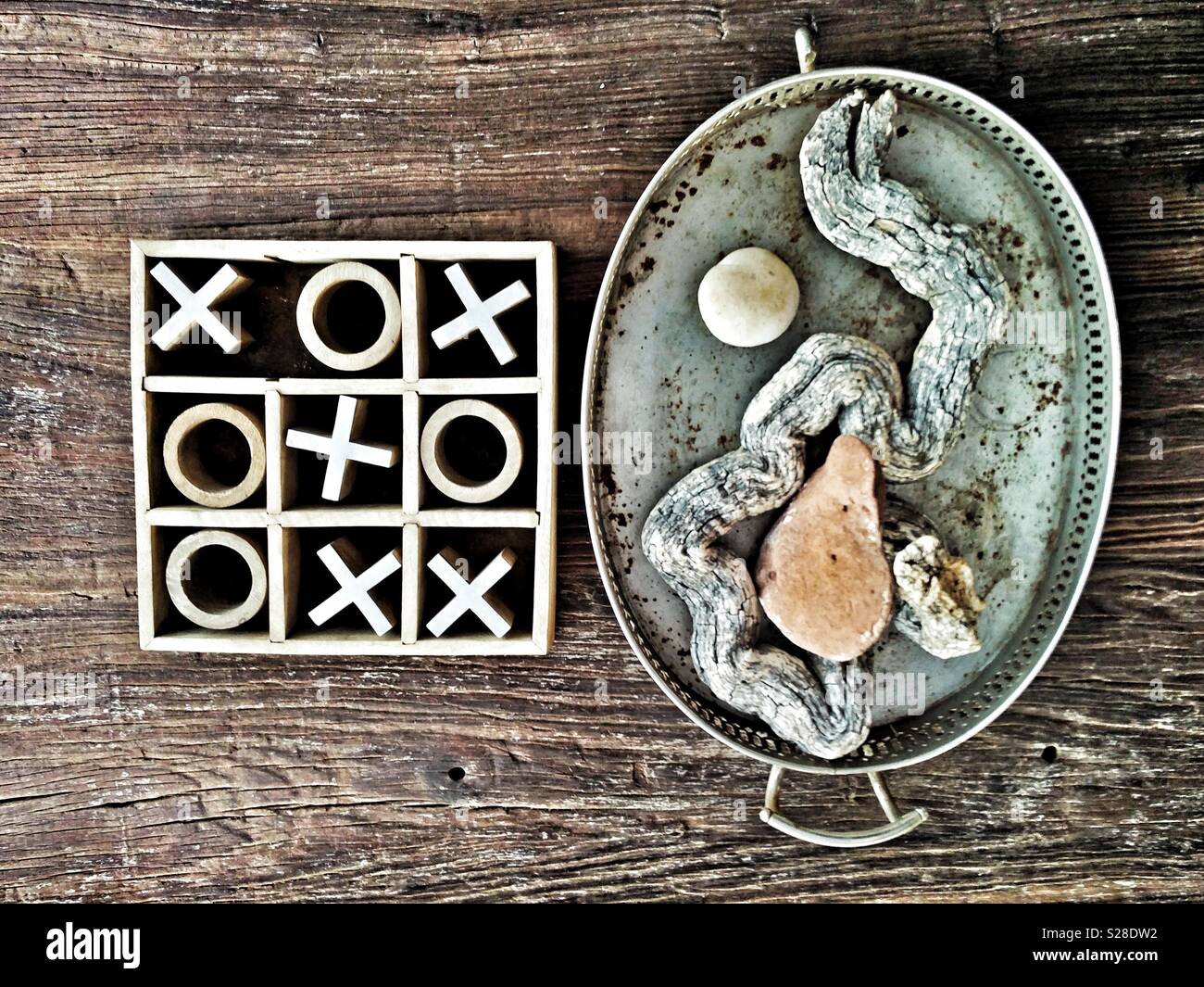 Noughts and crosses or tic-tac-toe children's game next to a decorative tray of objects on a grainy tabletop. Crosses win. Stock Photo