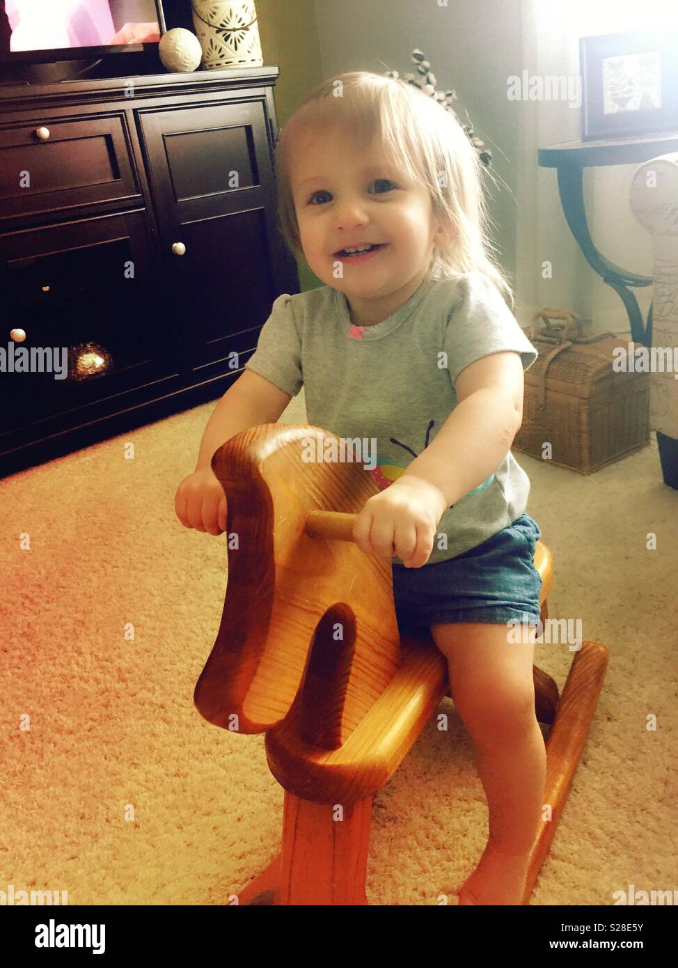 One and ahalf year old blonde girl riding a vintage rocking horse, USA - Smartphone Captured Stock Image