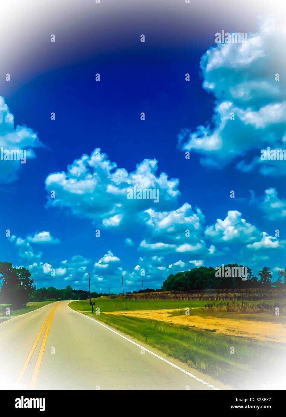 Blurred photo of fluffy cumulus clouds over rural North Carolina fields and road - Smartphone Captured Stock Image