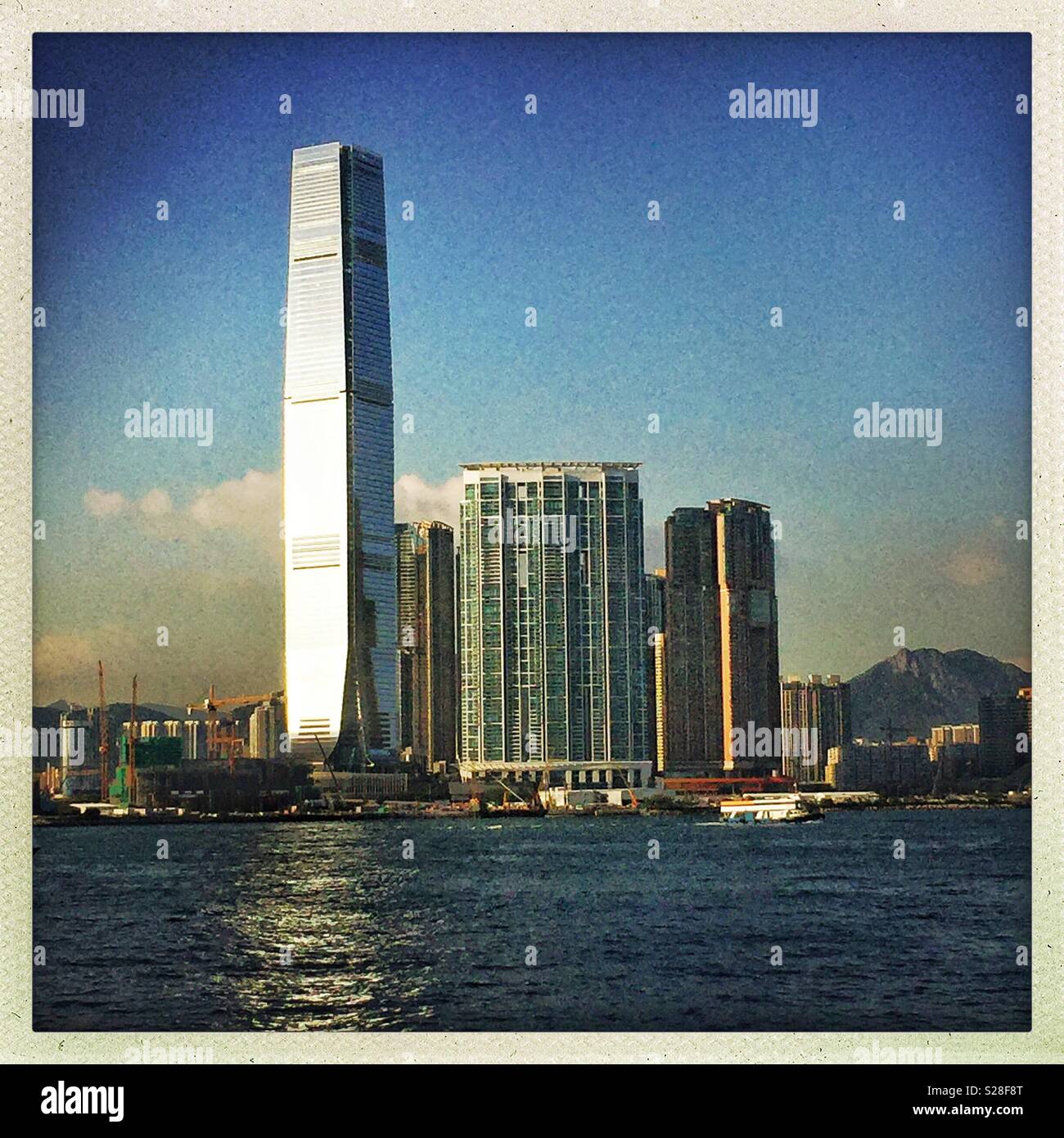 Late afternoon sunlight reflected in the glass curtain wall of the ICC, Hong Kong's tallest building, and Victoria Harbour - Smartphone Captured Stock Image