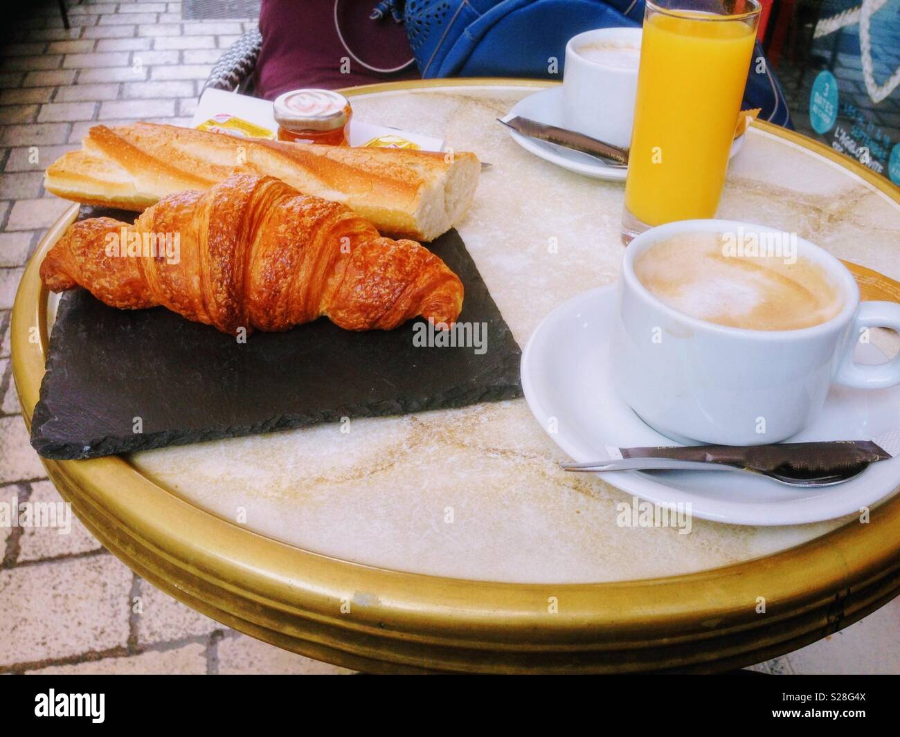 Enjoying  breakfast with croissant, fresh bread, and coffee at a sunny cafe terrace - Smartphone Captured Stock Image