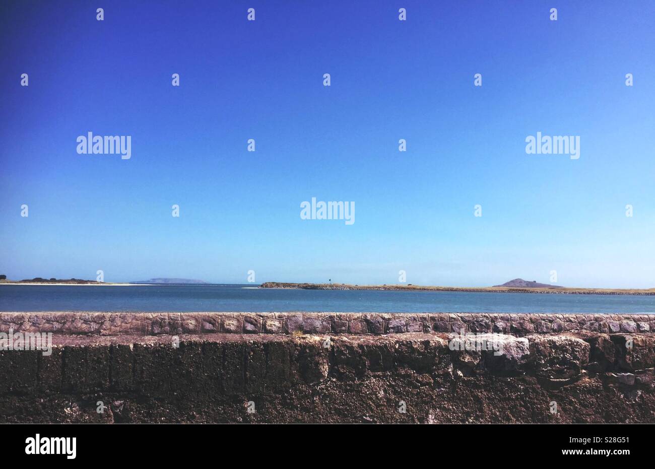 Peering over the wall an almost blue sky with a small island on the horizon. A perfect background with room for text. - Smartphone Captured Stock Image