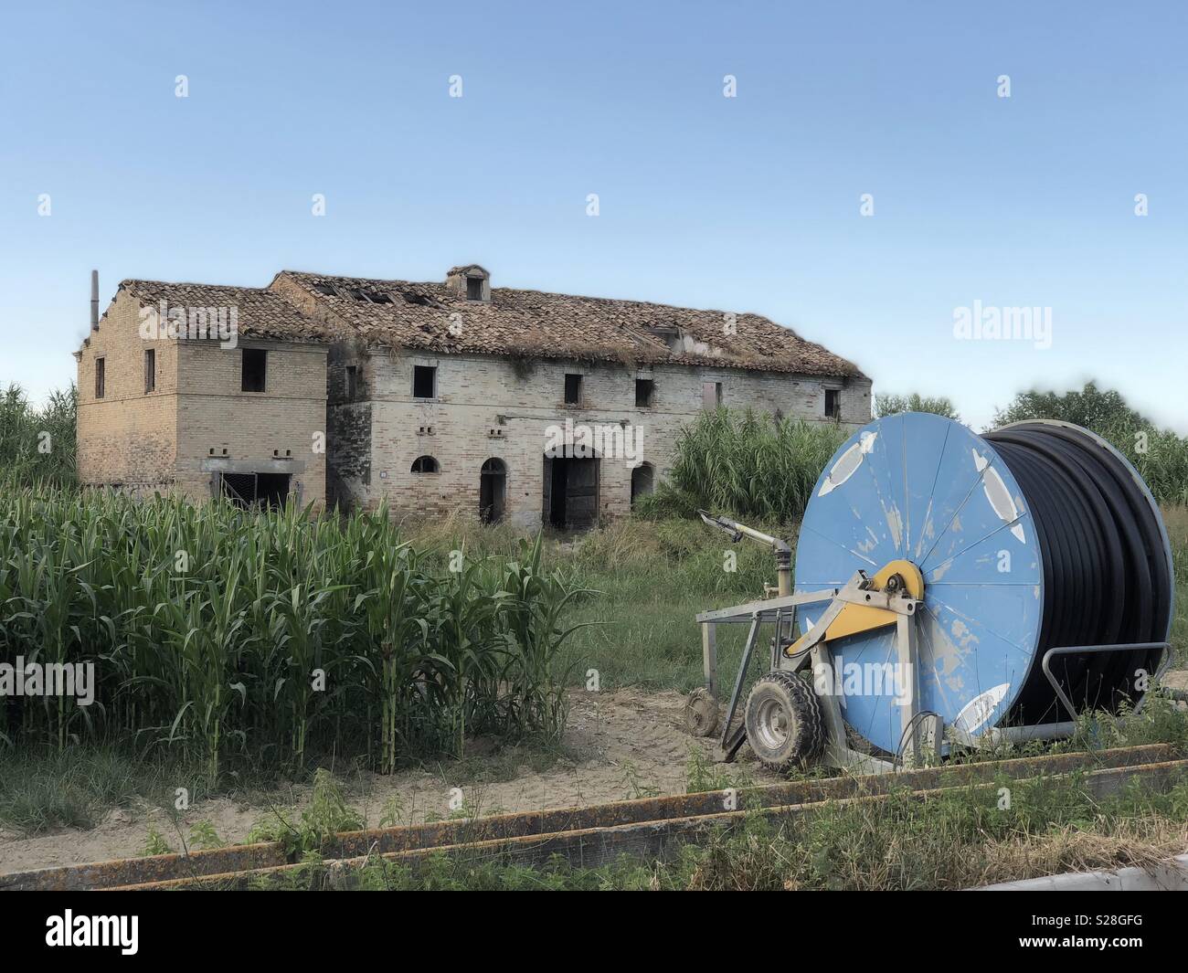 Irrigation machine front of a typical marche region country house abandoned in the Natural Park of Sentina, Italy Stock Photo