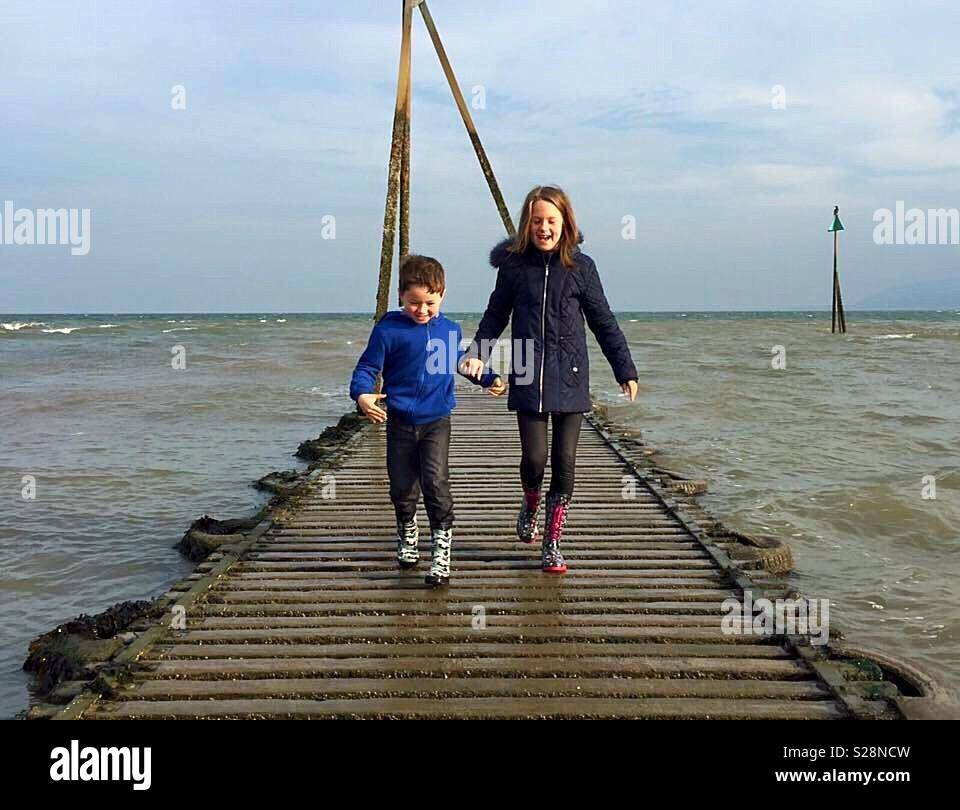 Brother and sister walking along a jetty in the sea Stock Photo - Alamy