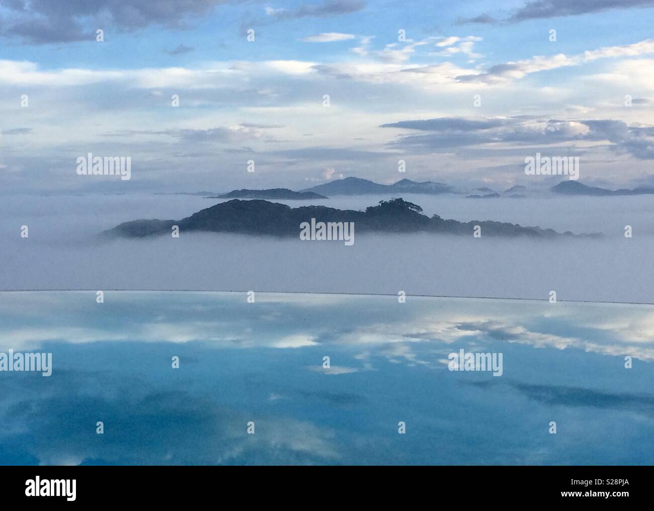 Morning landscape and sky with low cloud and hills reflected in infinity pool Stock Photo