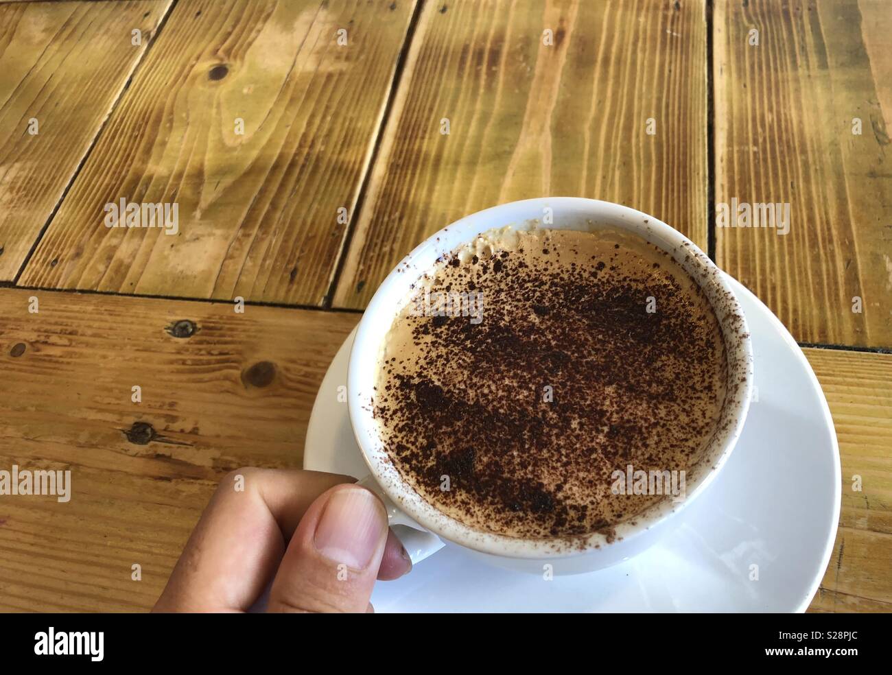 Asian hand holding cup of hot drink on wooden table - Smartphone Captured Stock Image