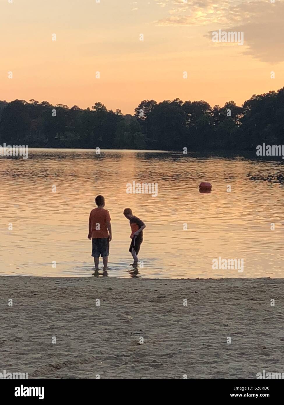 Two boys standing in lake at sunset Stock Photo - Alamy