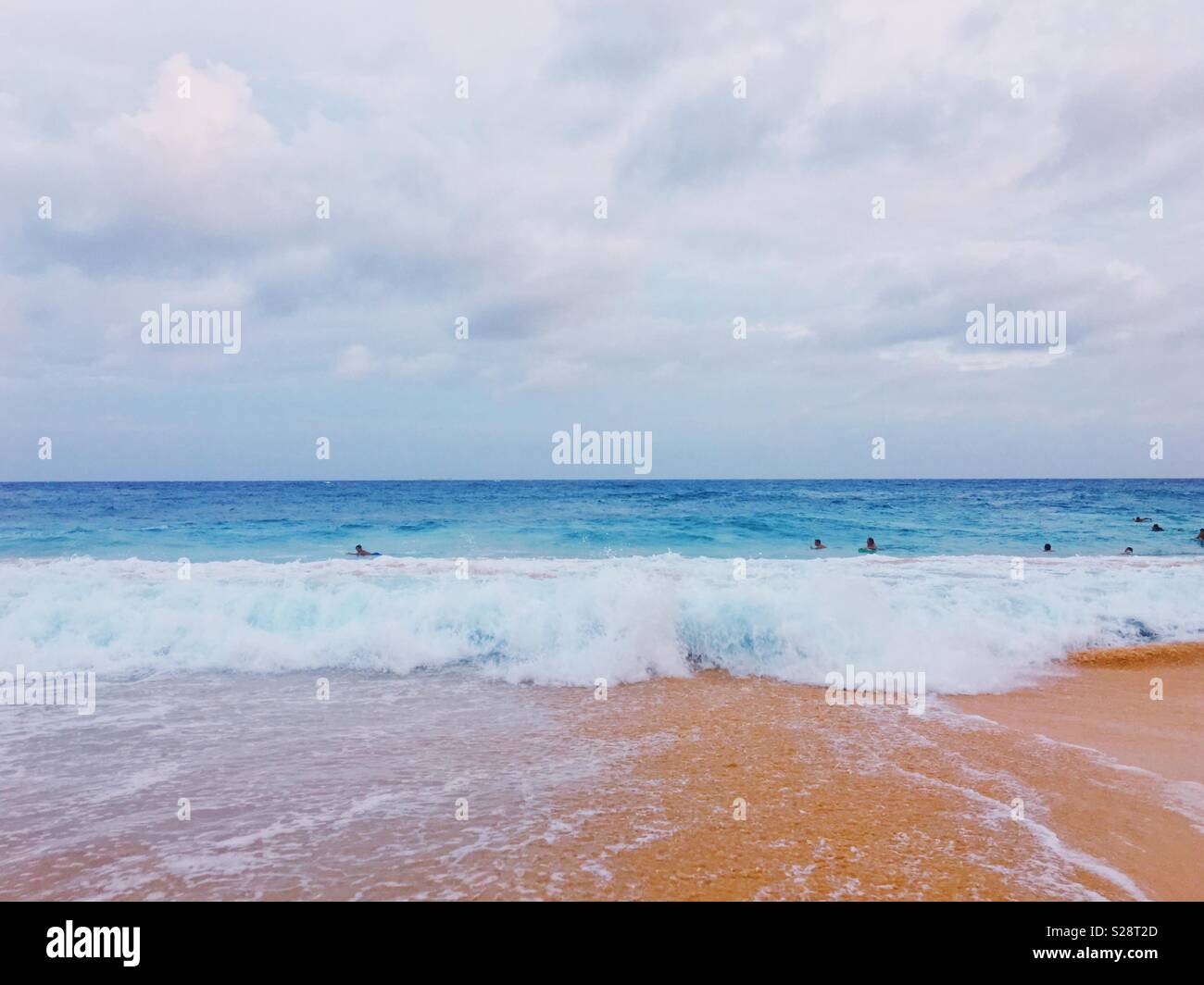 Looking out at sea from a sandy beach with surfers and boogie boarders in the water. - Smartphone Captured Stock Image