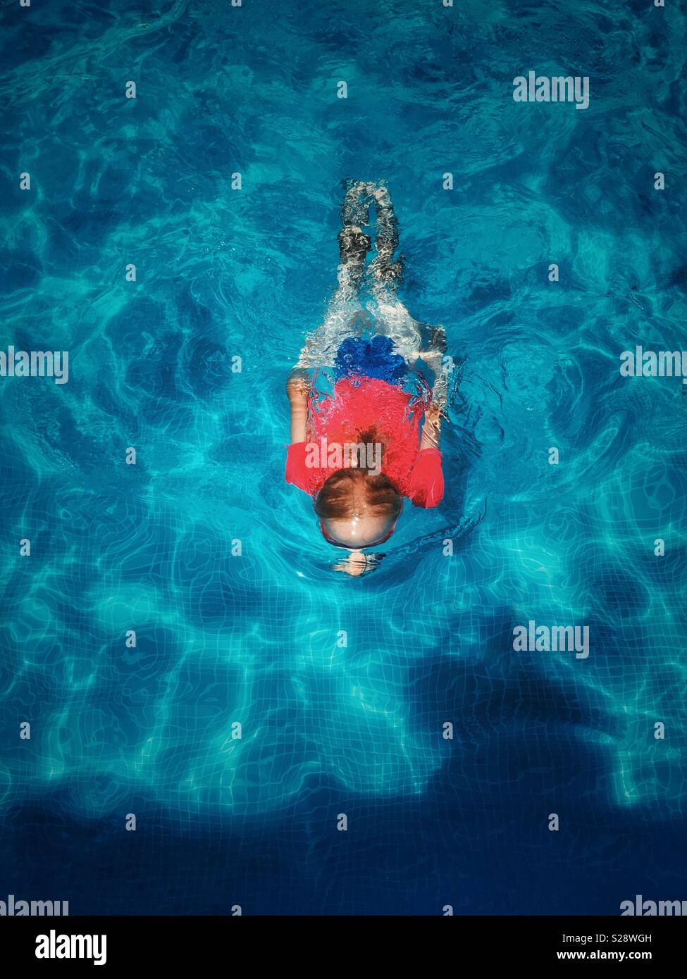 Girl in red top swimming under water in blue swimming pool Stock Photo