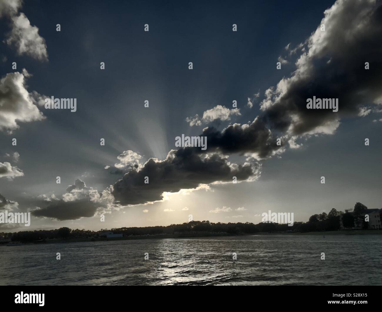 Sunset with sun behind clouds. Grey picture with a touch of colour in the clouds. In front is a Lake and trees in the back - Smartphone Captured Stock Image