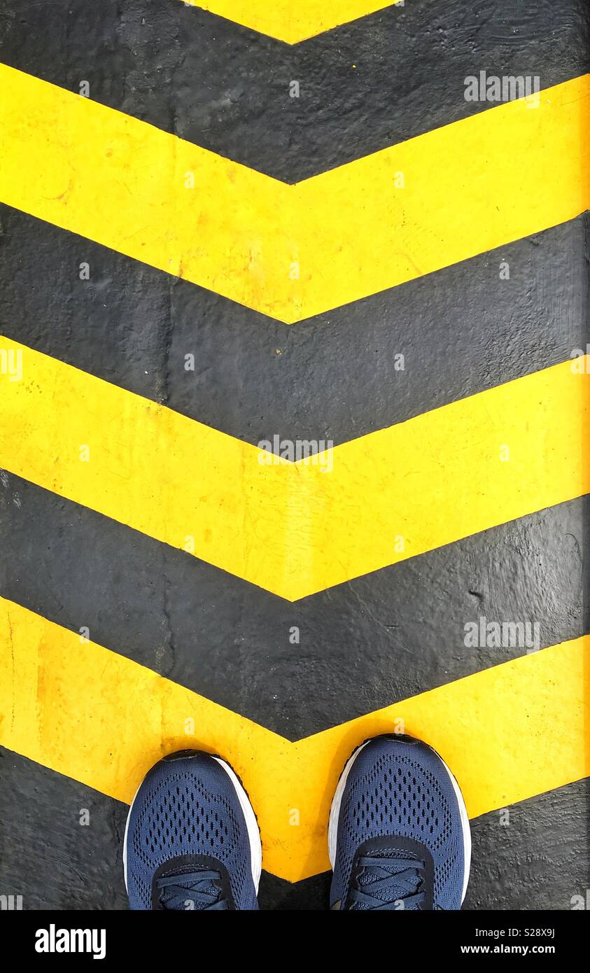 Direction concept. Yellow and black painted arrows look at shoes standing on them. - Smartphone Captured Stock Image