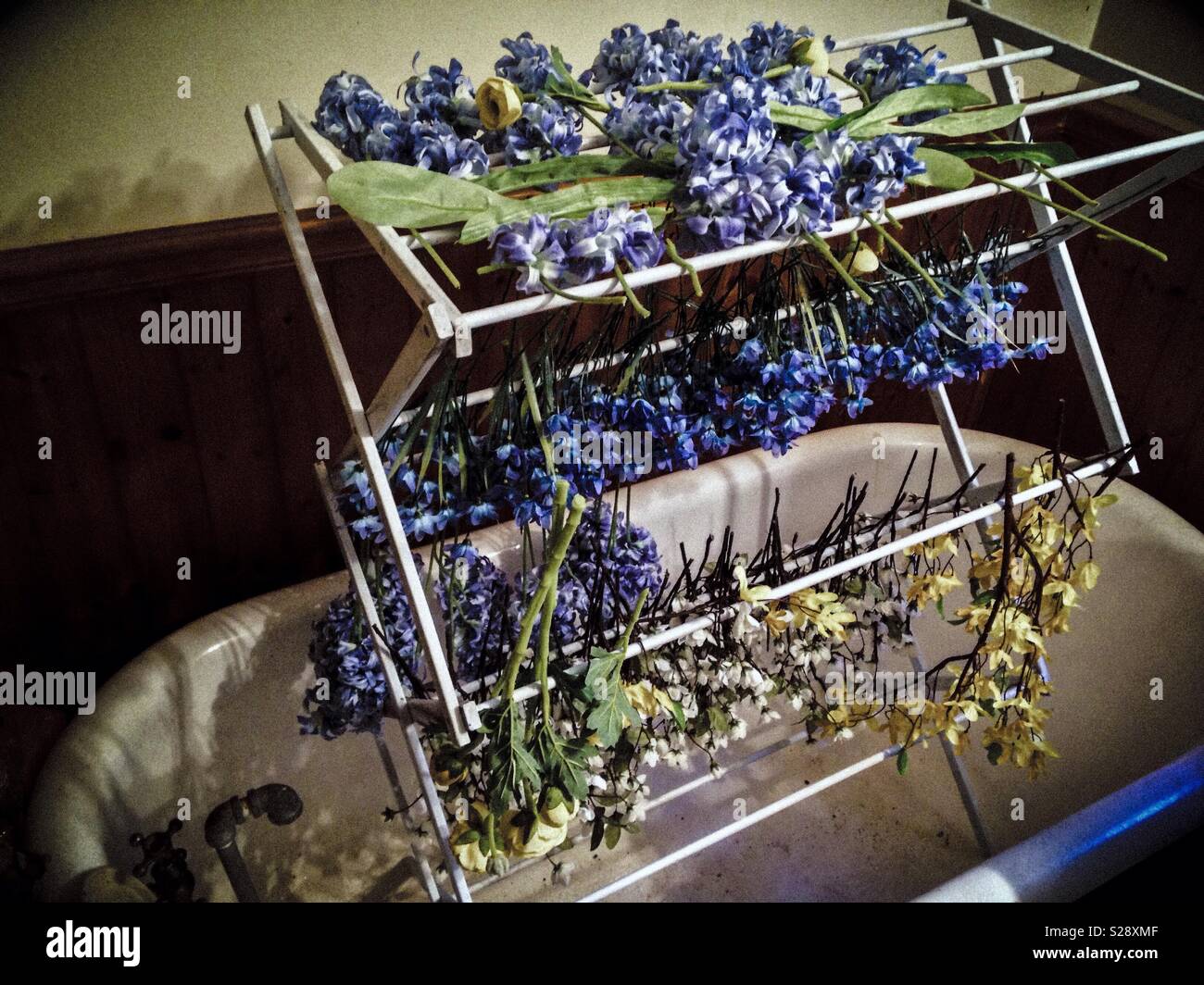 Shadowy photo of silk flowers hanging to dry on a wooden rack in a cast iron tub after a soapy washing - Smartphone Captured Stock Image