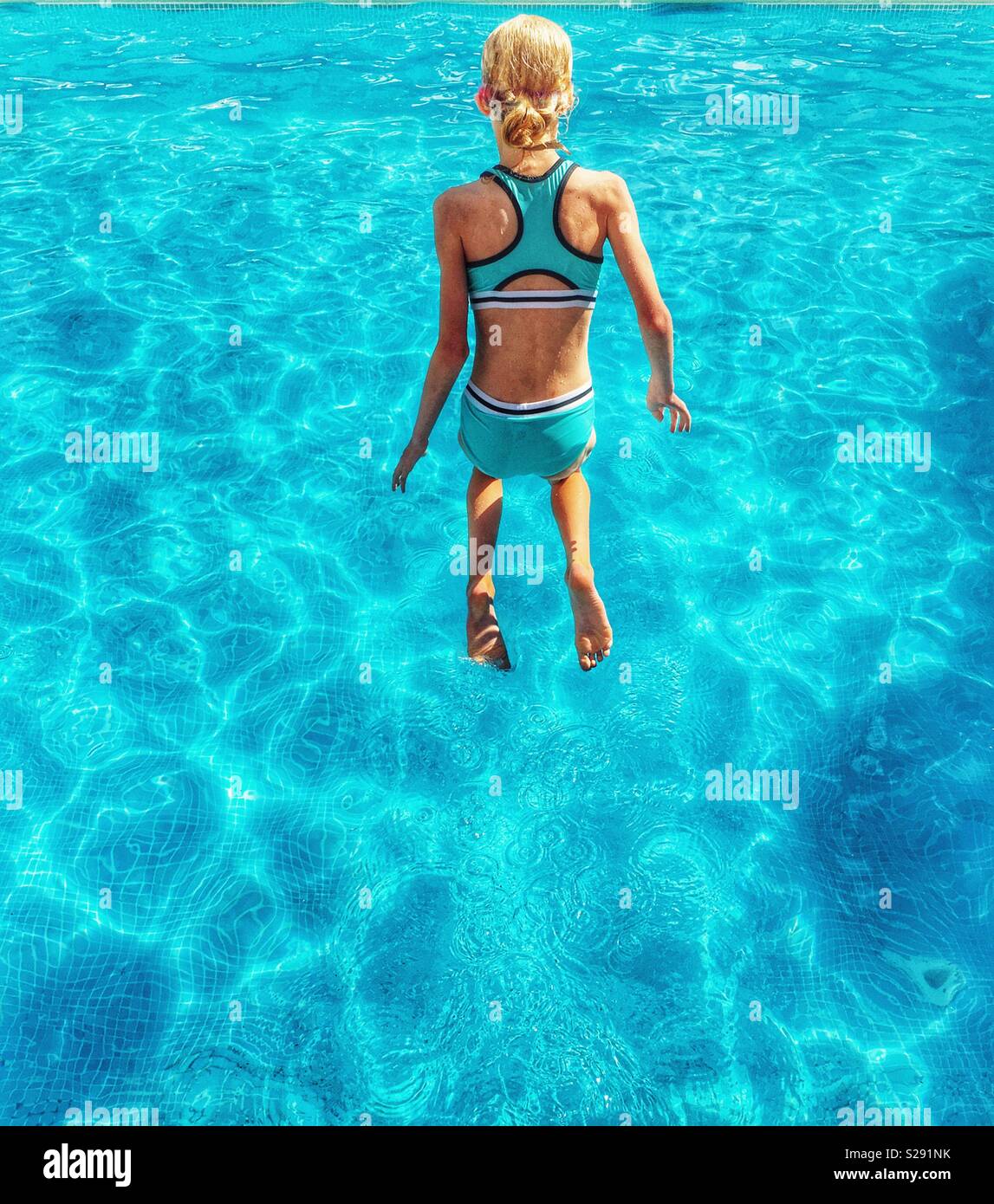 Young girl in blue swimming costume jumping into blue pool Stock Photo