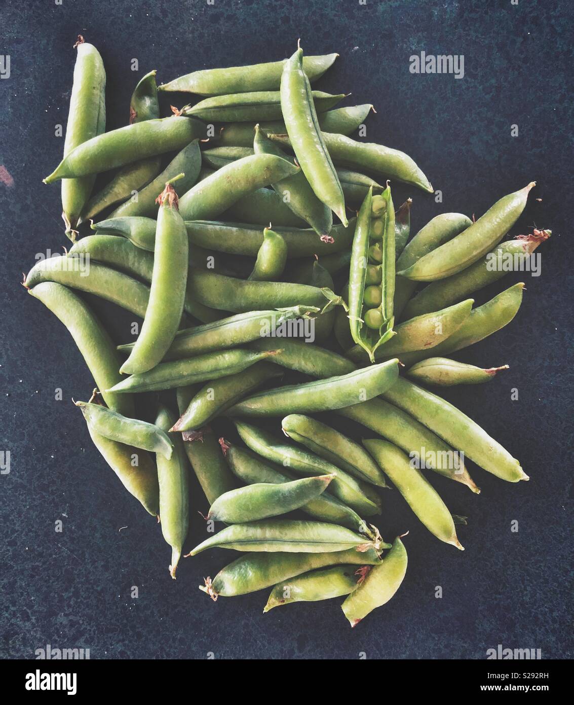 Fresh harvest of peas in a pod on a dark kitchen counter Stock Photo