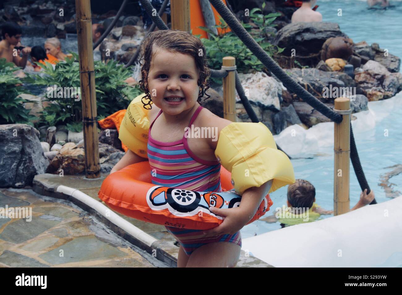 Little girl wearing a swim ring and arm bands at a swimming pool Stock