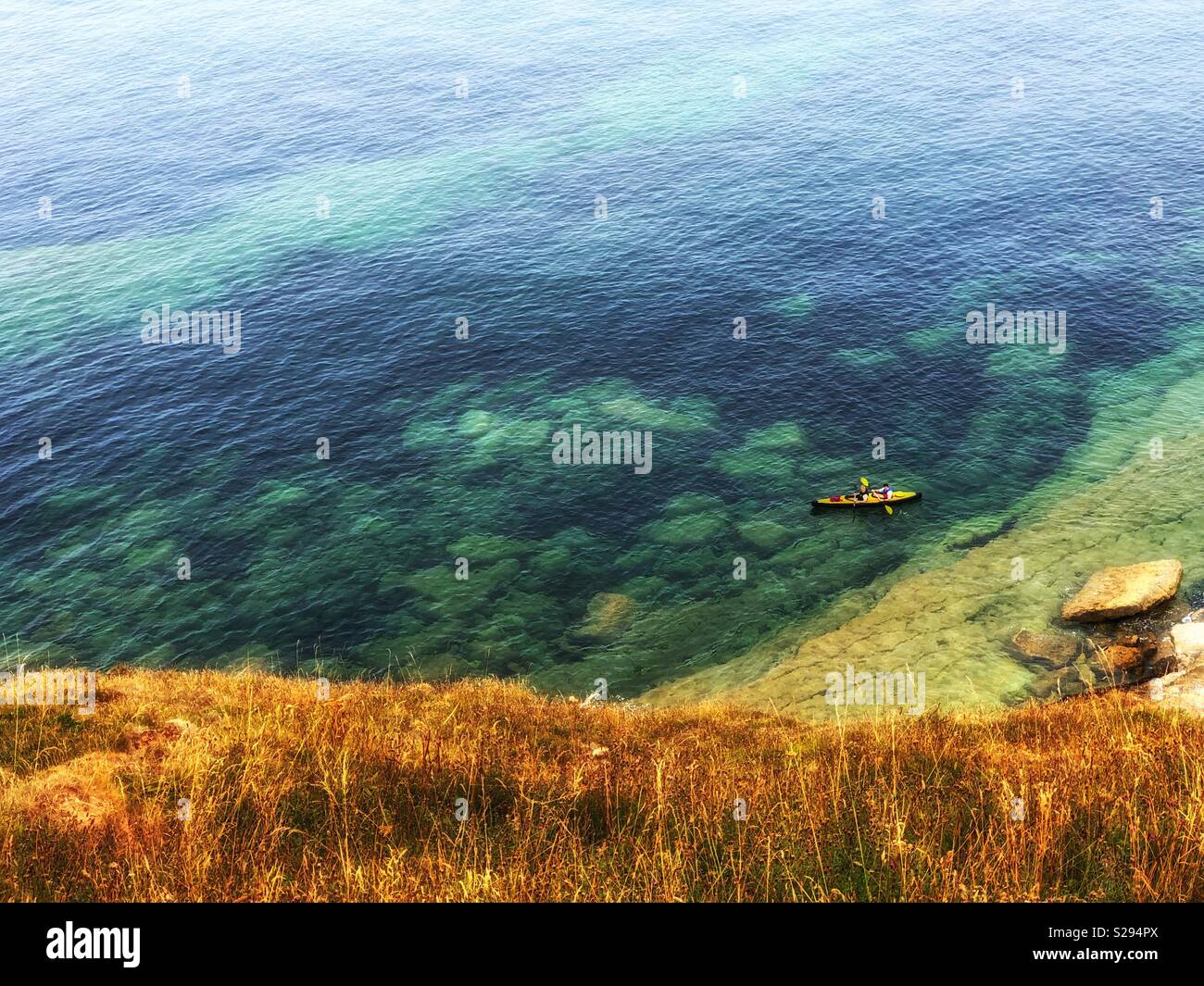 Looking down on two people in a kayak paddling in shallow water around the coast - Smartphone Captured Stock Image