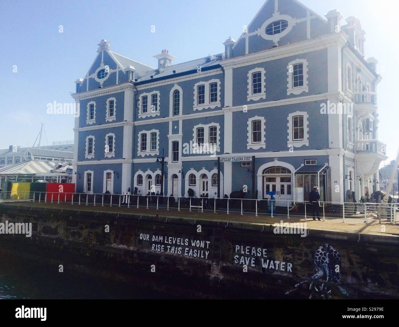 Beautiful old building at V&A Waterfront in Cape Town with graffiti slogan on the wall beneath urging everyone to save water due to the ongoing drought Stock Photo