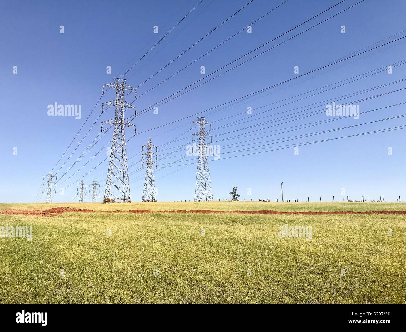 High voltage towers over a green field and against clear blue sky - Smartphone Captured Stock Image
