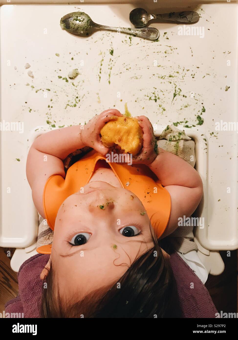 Overhead view of a baby girl sitting in a high chair eating a peach. Stock Photo