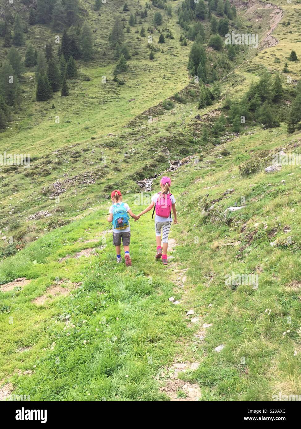 Sisters walking hand in hand on a mountain trail. - Smartphone Captured Stock Image