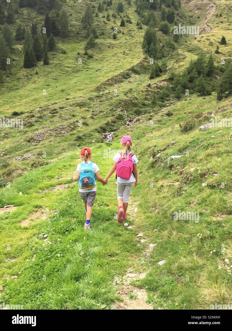 Sisters walking hand in hand on a mountain trail. - Smartphone Captured Stock Image