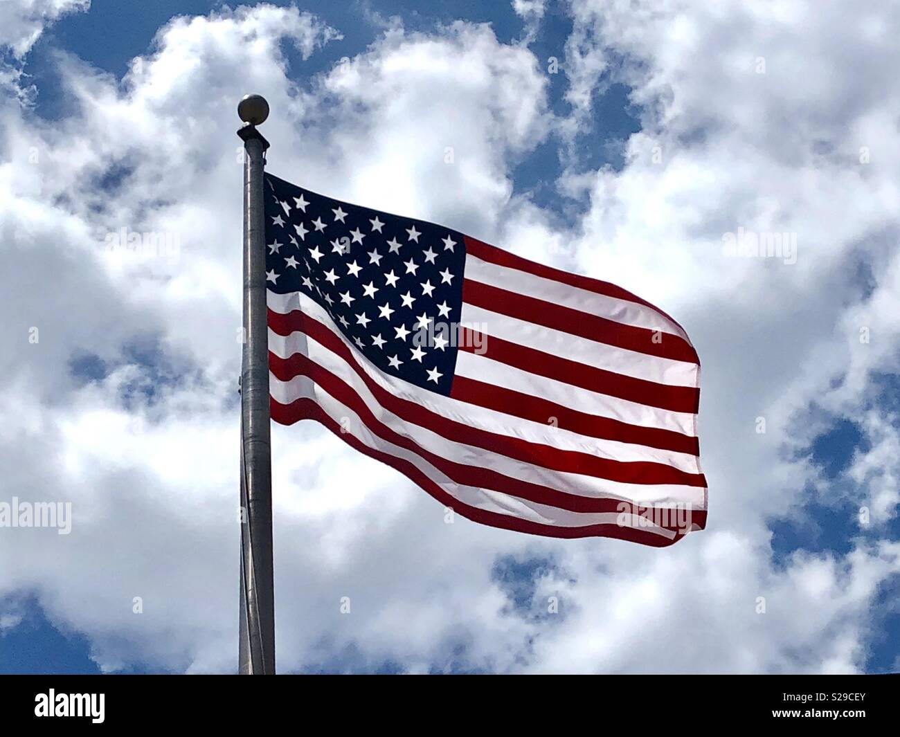 American flag flying against a blue sky with clouds - Smartphone Captured Stock Image